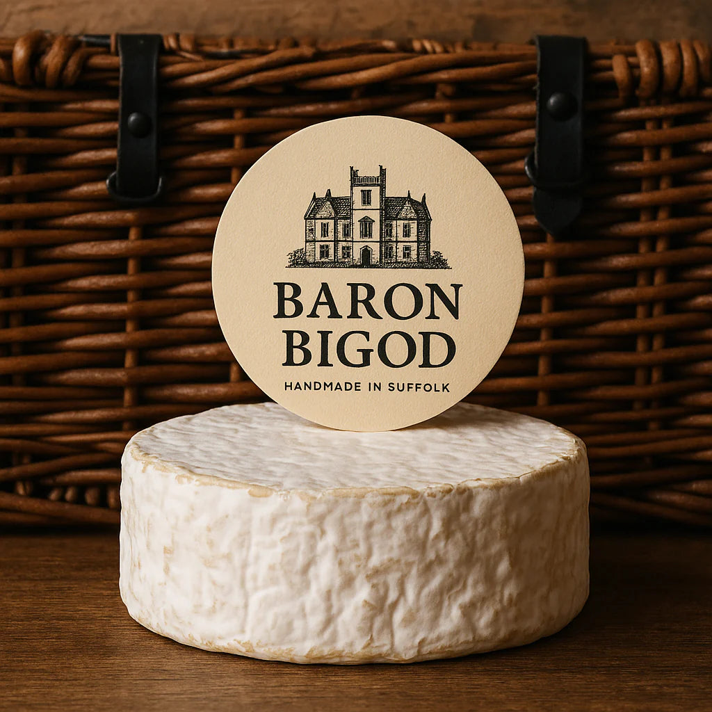 Wheel of Baron Bigod artisan brie-style cheese resting on a rustic wicker hamper, showcasing its creamy rind and traditional packaging.